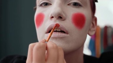 Soytarı makyajı yaparken dudaklarını fırçayla kırmızıya boyayan Z jenerasyonunun aşırı yakın plan portresi.