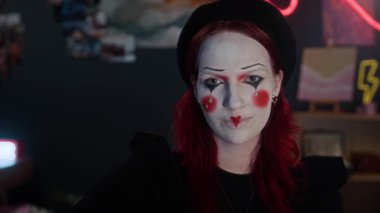 Yaratıcı pandomimci kız, siyah şapka, kırmızı eldivenler ve loş ışıklı odada kameraya poz veren el aksesuarları takan Kafkasyalı gen Z kızı.