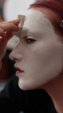 Beyaz yüz boyasını süngerle dikkatlice harmanlayan beyaz kadın amatör makyaj sanatçısının dikey yakın çekimi