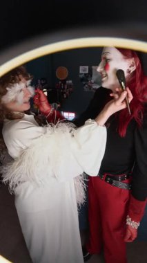 Yaratıcı makyaj yapmış fırça kullanıyormuş gibi yapan, sohbet eden ve görünüşlerine hayran olan iki kadının dikey çekimi.