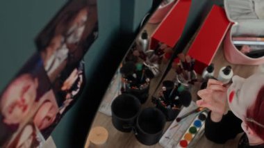 Neşeli Z neslinin yüksek açılı portresi kırmızı dudak boyayan ve palyaço makyajı yaparken kameraya üfleyen kız makyaj masasına bak.