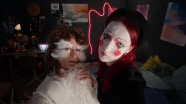 UGC 'de iki yaratıcı bayan arkadaşın resmi var. Biri yüzünde tüyler olan beyaz elbiseli, diğeri ise palyaço makyajlı siyah ve kırmızı elbiseli, oyuncu dramatik bir hava yayıyor.