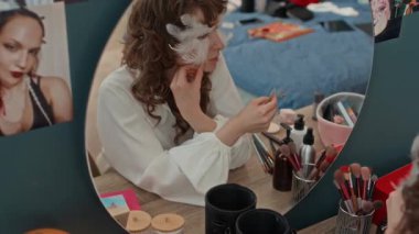 Yüzünde dekoratif tüyler olan, makyajına inci çıkartmalar ekleyen, yuvarlak beyaz kadın aynasından yukarıya bak.