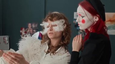 Genç kostüm bayan arkadaşları melek ve pandomimci gibi görünüyor. Evdeki akıllı telefonun ön kamerasına poz veriyorlar.