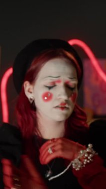 Kırmızı saçlı, pandomimci kız ve siyah eldivenli siyah şapkalı siyah kızın dikey portresi karanlık odada kameraya çarpıcı bir şekilde bakıyor.