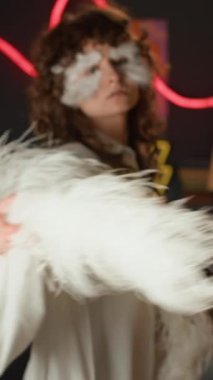 Dikey odak noktası, uzun kıvırcık saçlı, beyaz elbiseli, kameraya poz veren, dekoratif tüyleri ve inci elmasları olan yaratıcı makyaj yapan genç bir kadının portresi.