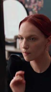 Dikey olarak genç bir kadının kızıl saçlarını düzeltmesi ve makyajını kontrol etmesi dışarı çıkmaya hazırlanırken aynada kendine bakması.