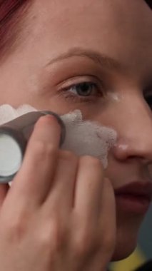 Z jenerasyonundaki kızın kostüm partisine hazırlanırken beyaz zemini boya çubuğuyla cilde uyguladığı dikey yakın çekim.