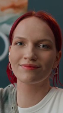 Sosyal medya için makyaj dönüşümlü kızıl saçlı genç bir kadının dikey UGC görüntüsü. Sonuç olarak palyaço makyajı yapıyor.