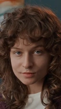 Septum piercingli kızın dikey poziyonu yüzünde tüyler ve mücevherlerle melek görünüşü yarattıktan sonra makyaj dönüşümünü gösteren video kaydı.