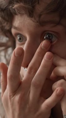 Doğal kıvırcık saçlı ve burnu delinmiş genç bir kadının dikey yakın plan fotoğrafı. Gözüne koyu renk lens takıyor.