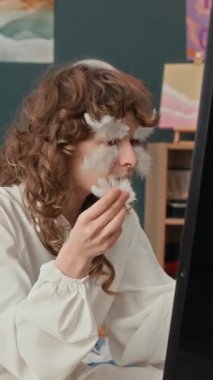 Z jenerasyonunun dikey görüntüsü kıvırcık saçlı kız kostümlü partiye hazırlanırken aynanın karşısına dekoratif tüyleri dikkatlice yapıştırıyor.