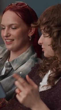 Hafta sonunu evde geçirirken akıllı telefondan iletişim kuran ve bilgi arayan iki pozitif bayan arkadaşın dikey görüntüsü