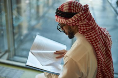 Genç Arap işadamının ofiste otururken belgelere bakarken orta açıdan çekilmiş bir fotoğrafı.