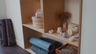 Sağlıklı aksesuarlı ahşap raflar ve yoga minderleri, masaj topları, mumlar ve minimalist spor salonunda havluları olan hasır sepetler de dahil olmak üzere spor aletleri.