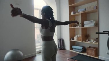 Spor kıyafetleriyle siyah bir kadının modern spor salonunda kol daireleri çizdiğini ve omuzlarını esnettiğini hayal edin.