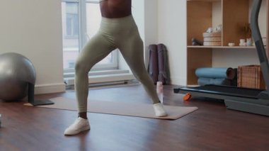 Spor kıyafetli siyahi bir kadının spor giyim kuşamında kollarını yukarı doğru uzatarak atlama hareketini çek.