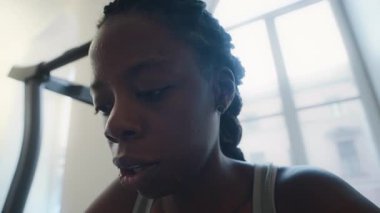 Yorgun siyah kadının derin nefes alışını ve evdeki yoğun koşu bandı egzersizinden sonra yüzündeki teri havluyla silmesini yakından izleyin.