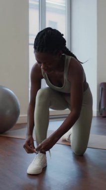 Spor kıyafetli, spor ayakkabılı, spor ayakkabılı bir kadının spor salonuna girmeden önce spor ayakkabılarını bağlarken dikey pozu.