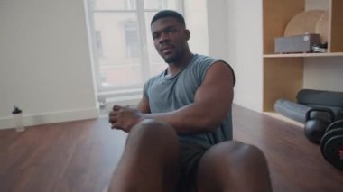 Atletik siyahi adam evde sakızla vücut kaslarını çalıştırırken egzersiz minderinde Rusça kıvrımlar yapıyor.