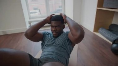 Spor elbiseli kaslı Afrikalı Amerikalı adam spor salonunda paspas üzerinde egzersiz yaparken ellerini başının arkasına kıvırıp kıvırıyor.