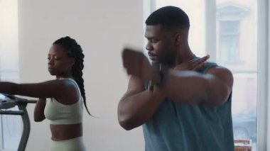 Siyah fitness antrenörü, spor salonunda antrenman yaparken genç bayana kol dairesi egzersizi yapıyor.