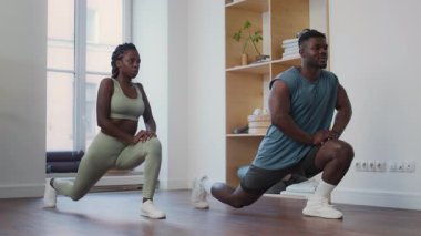 Modern minimalist jimnastik salonunda genç bir bayanla kişisel antrenman yaparken kaslı siyah fitness eğitmeni hamleyi nasıl yapacağını anlatıyor.