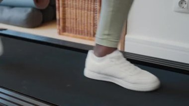 Genç Afrikalı Amerikalı bir kadının spor kıyafetleri ve spor ayakkabıları içinde koşu bandında yürürken ev jimnastiği yaparken çekimini kaldır.
