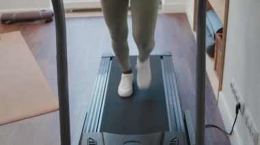 Aktif giyimli genç Afrikalı Amerikalı kadının evdeki kardiyo çalışması sırasında koşu bandında koşarken çekimini kaldır.