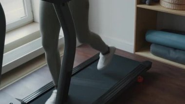 Spor giyimli siyah bir kadının evdeki kardiyo antrenmanı sırasında koşu bandında koşarkenki görüntüsü.