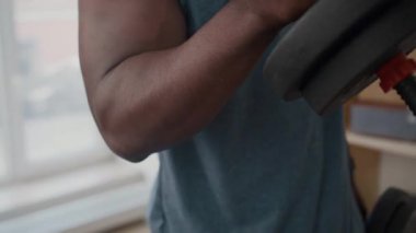 Kas gücü olan siyah bir adamın ev egzersizi sırasında dambıl gibi kıvrımlar yapmasını yakından izleyin.