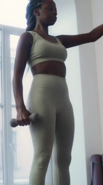 Spor salonunda spor yaparken spor yapan Afro-Amerikan bir kadının dambıl önünde yaptığı dikey eğik çekim.