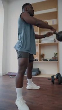 Güçlü Afro-Amerikan bir adamın, spor salonunda ağırlıklarla antrenman yaparken arka arkaya kettlebell sallamasını çekiyoruz.