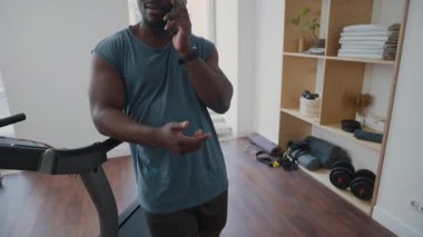 Spor salonundaki koşu bandının yanında duran ve spor yaptıktan sonra cep telefonuyla konuşan atletik zenciyi çek.