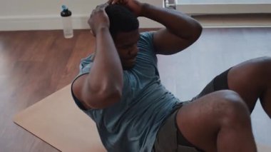 Spor giyim giymiş kaslı Afrikalı Amerikalı adam antrenman sırasında egzersiz minderinde mekik çekiyor.