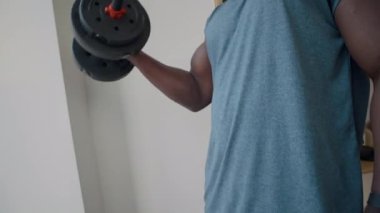 Spor giyim sektöründe genç bir zenci kablosuz kulaklıklarla müzik dinliyor ve spor salonunda egzersiz yaparken tek kollu halterler sallıyor.