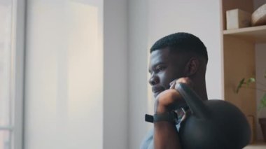 Güçlü, kaslı kollu, ağırlık kaldırma egzersizi sırasında tek kollu, kettlebell presi yapan Afrikalı Amerikalı bir adam.