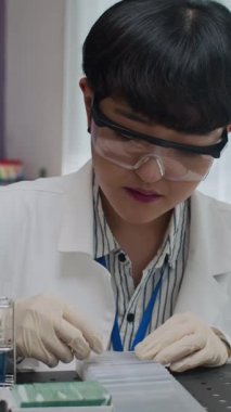 Dikey çekimde gözlüklü ve lateks eldivenli Asyalı bilim adamı örnek ile slayta bakıyor.