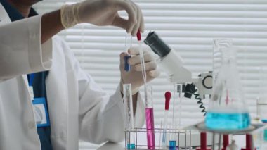 Tanımlanamayan erkek bilim adamı pipeti kullanarak test tüpüne koyu mavi sıvı koyuyor.