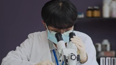 Çalışma masasında oturan genç kadın bilim adamı mikroskopla incelerken petri kabında numune ayarlıyor.