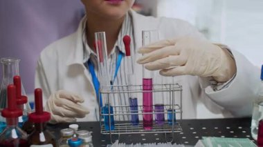 Laboratuvar uzmanı, laboratuardaki masada bulunan metal kutudan mor sıvıyla uzun bir test tüpü alıyor.