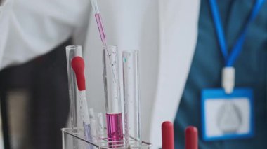 Bakteri yetiştirmek için petri kabına leylak sıvısı eklemek için cam pipet kullanan tanımlanamayan erkek elinin görüntüsü.