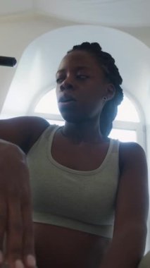 Yorgun Afrikalı Amerikalı kadının derin nefes alışını ve antrenman sonrası spor salonunda su içişini dikey açıdan çekiyoruz.