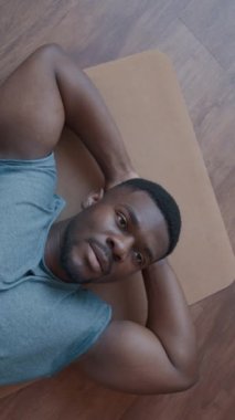 Spor sonrası iyileşme sürecinde spor minderinde elleri başının arkasında dinlenen kaslı siyahi bir adamın kamera görüntüsü.