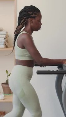 Dikey olarak siyah bir kadının koşu bandında yürüdüğü, sonra hızlı adımlar attığı ve spor salonunda kardiyo çalışması yaptığı bir sahne.