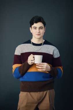 Siyah arka planda duran ve kahve içen genç bir çalışanın portresi.