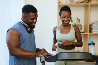 Modern spor salonlarında koşu bandında spor yapan gülümseyen bir çift. Mutlu ve egzersiz rutinlerine odaklanmış görünüyorlar.