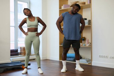 Afrika kökenli Amerikalı çift spor kıyafetlerini giyip spor yaparken şık bir spor salonunda esneyip ısınıyorlar.