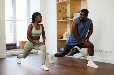 İyi ışıklandırılmış spor salonunda egzersiz yaparken bacaklarını esneten Afrikalı Amerikalı bir çift.