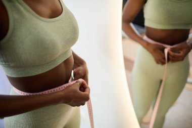 Yeşil aktif giysi giyerken, spor ve sağlığını korumaya odaklanarak bel ölçümü yapan bir kişinin yakın çekim görüntüsü